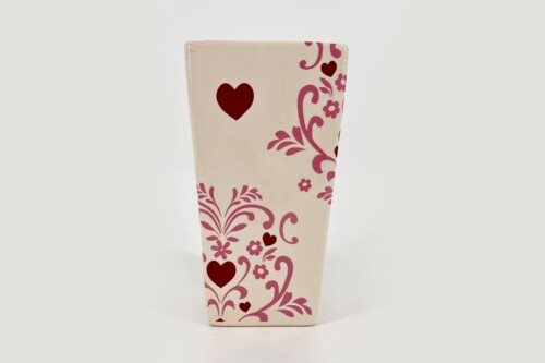 Tall cream-colored decorative vase with pink floral scrolls and red hearts on an off-white background