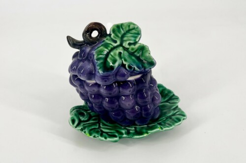 Glazed ceramic grape cluster with purple berries and glossy green leaves on a green base.