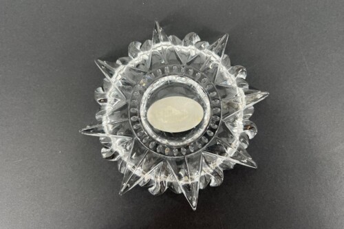 Clear glass starburst decorative candle holder with a round central reservoir on a dark background