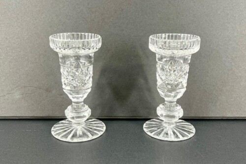Two crystal-cut goblets with faceted stems on a dark surface, standing side by side.