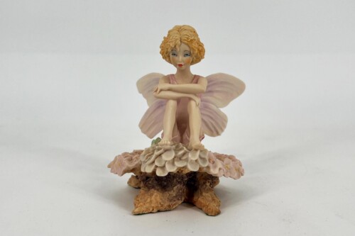 Tiny porcelain fairy figurine with curly blonde hair, pink dress, and pale wings, seated on a layered flower pedestal.