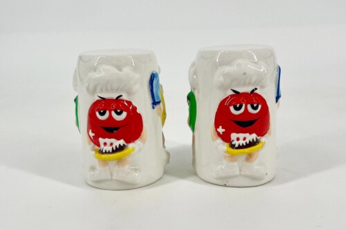 Two white ceramic salt and pepper shakers with red cartoon faces, yellow beaks, and colorful side accents standing side by side.