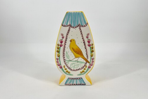 Decorative cutout shaped like a vase with a yellow bird in the center and blue striped top, framed by a floral border.