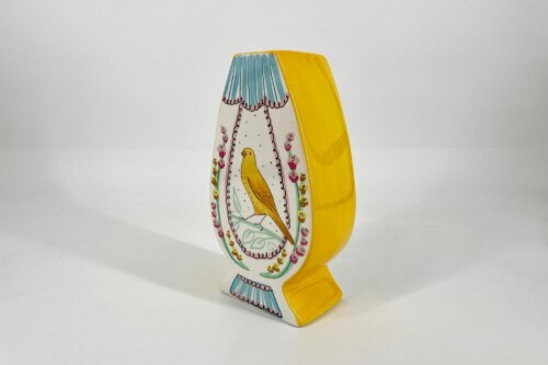 Yellow decorative ceramic sculpture with a painted oval scene: a yellow bird among pink flowers on a white panel with blue-striped top edge and bright yellow sides.