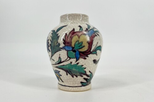 Ceramic vase with a crackled glaze and colorful floral pattern in green, blue, yellow, and red on a light background.