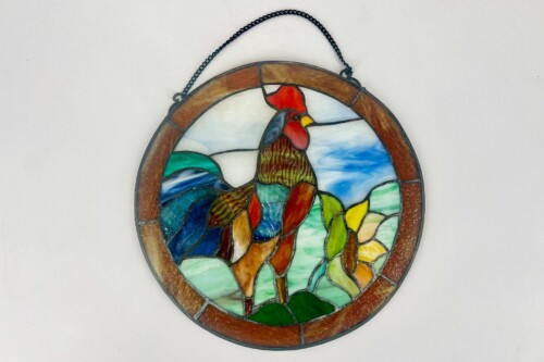 Circular stained-glass wall hanging showing a colorful rooster against a rural landscape with a brown outer ring and a metal chain hanger
