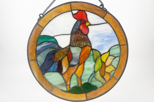 Circular stained-glass panel featuring a rooster in a colorful landscape with hills and fields, bordered by an amber ring.
