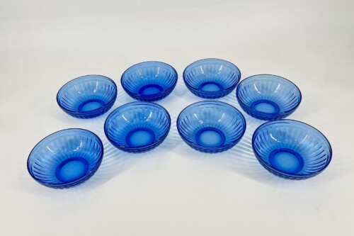 Eight cobalt blue ribbed glass bowls arranged in a rough circle on a white surface.]','