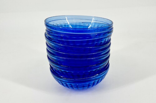 Blue ribbed glass vase with a curved, scalloped exterior on a white background.