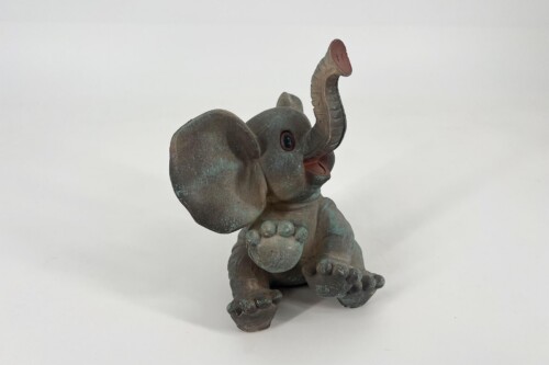 Bronze-green patina statue of a baby elephant with its trunk raised in a playful pose, front paws tucked under.