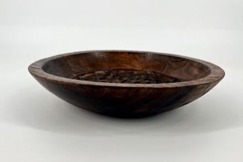 Shallow dark wooden bowl filled with loose tea leaves on a white surface