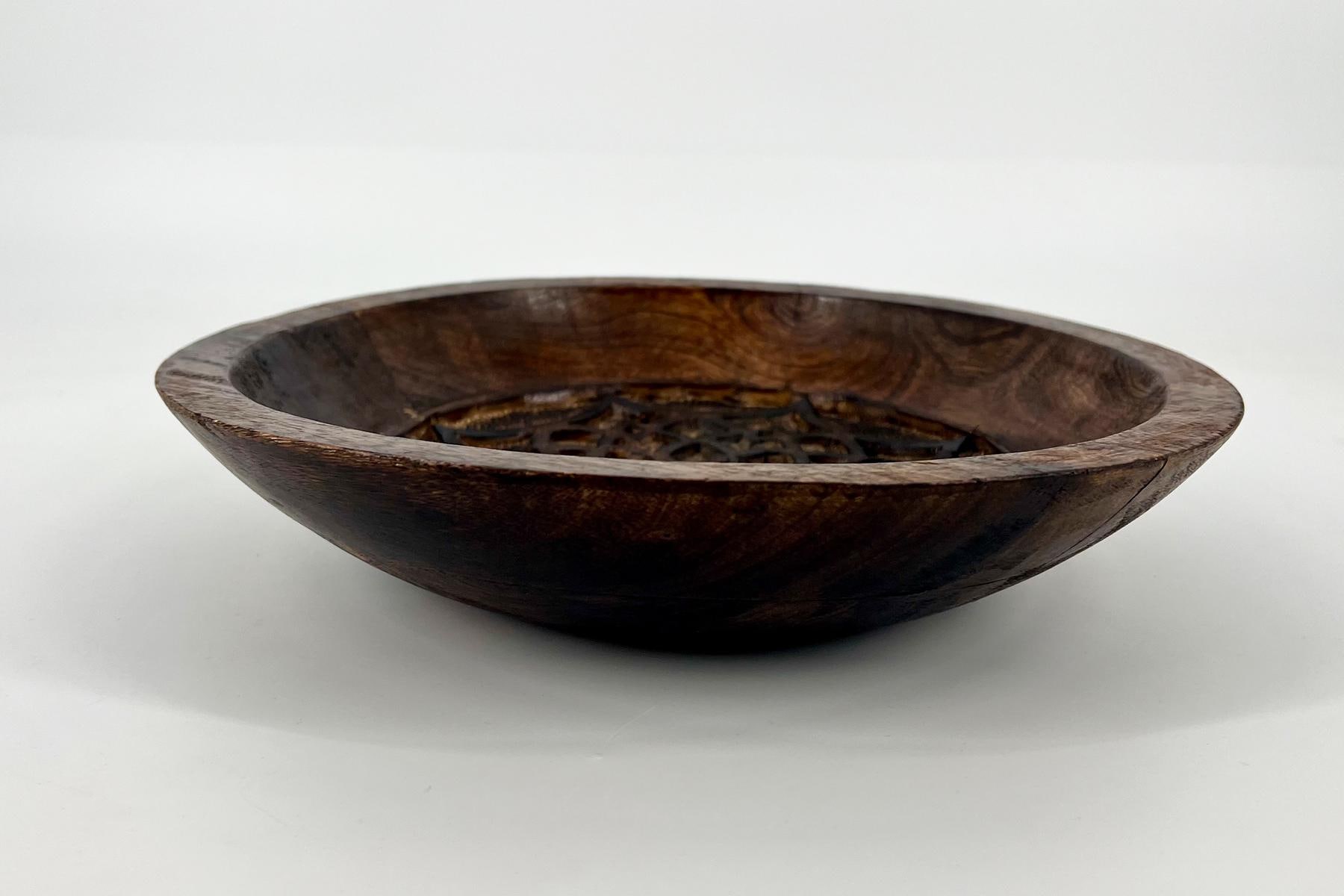 Shallow dark wooden bowl filled with loose tea leaves on a white surface