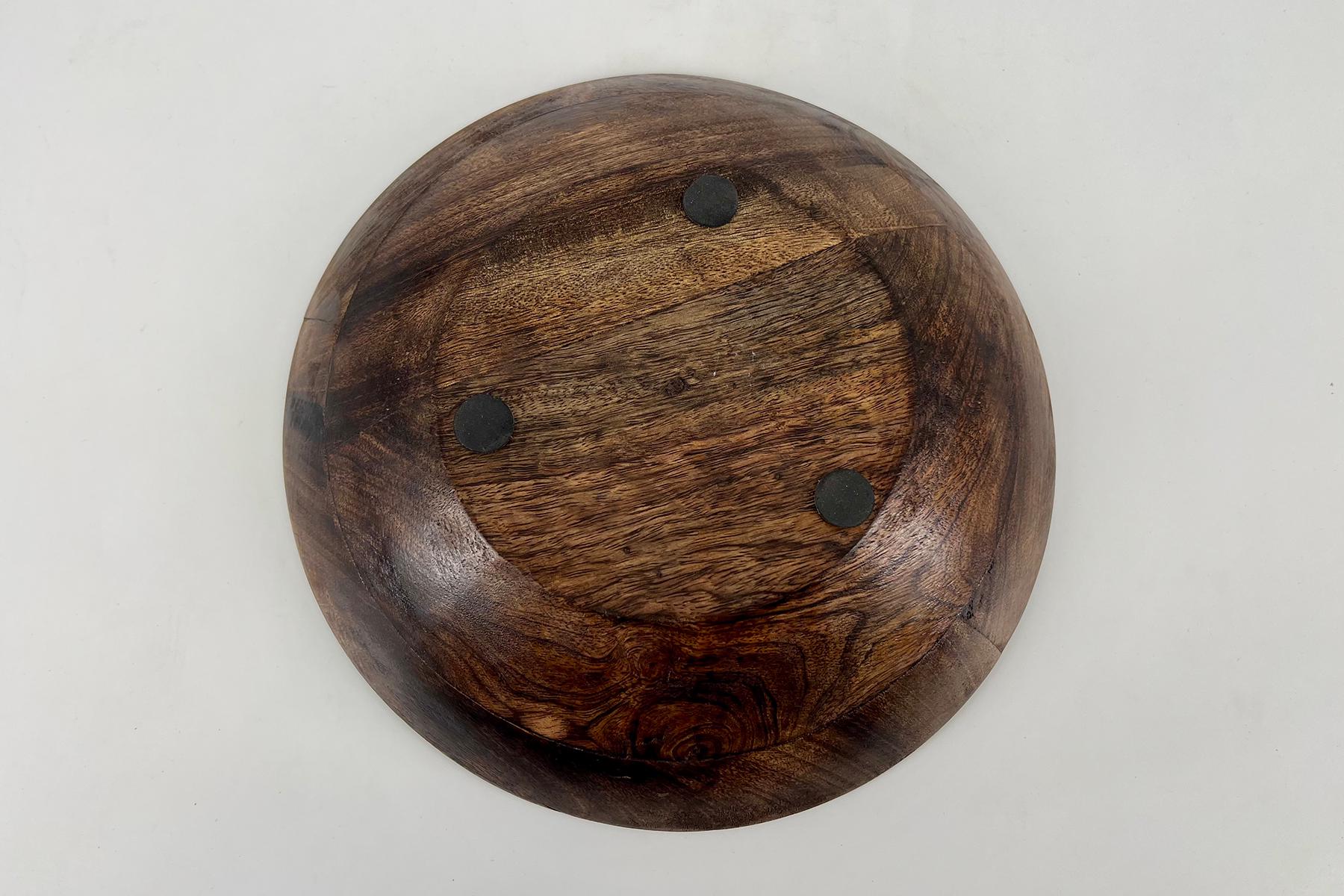 Top-down view of a dark brown wooden bowl with three black circular pads on the interior bottom.