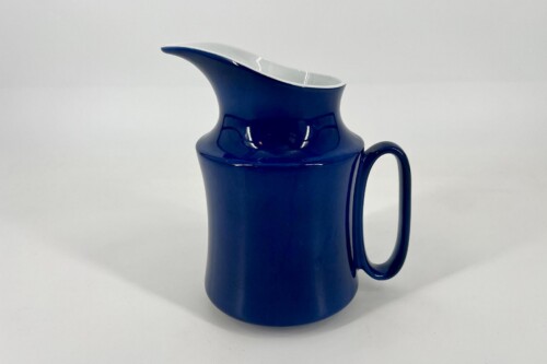 Blue ceramic pitcher with a white rim and curved handle against a white background, centered in the frame.