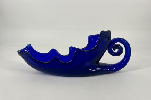 Blue glass sculpture shaped like a flowing wave with a curled tail, set on a white background.