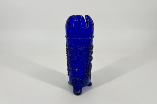 Cobalt blue glass sex toy shaped like a phallus, standing upright with a ribbed textured surface and bubble-like decorations on the shaft against a white background.