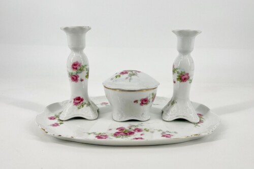 White porcelain centerpiece with two rose-pattern candlesticks and a small lidded dish on a matching floral plate.