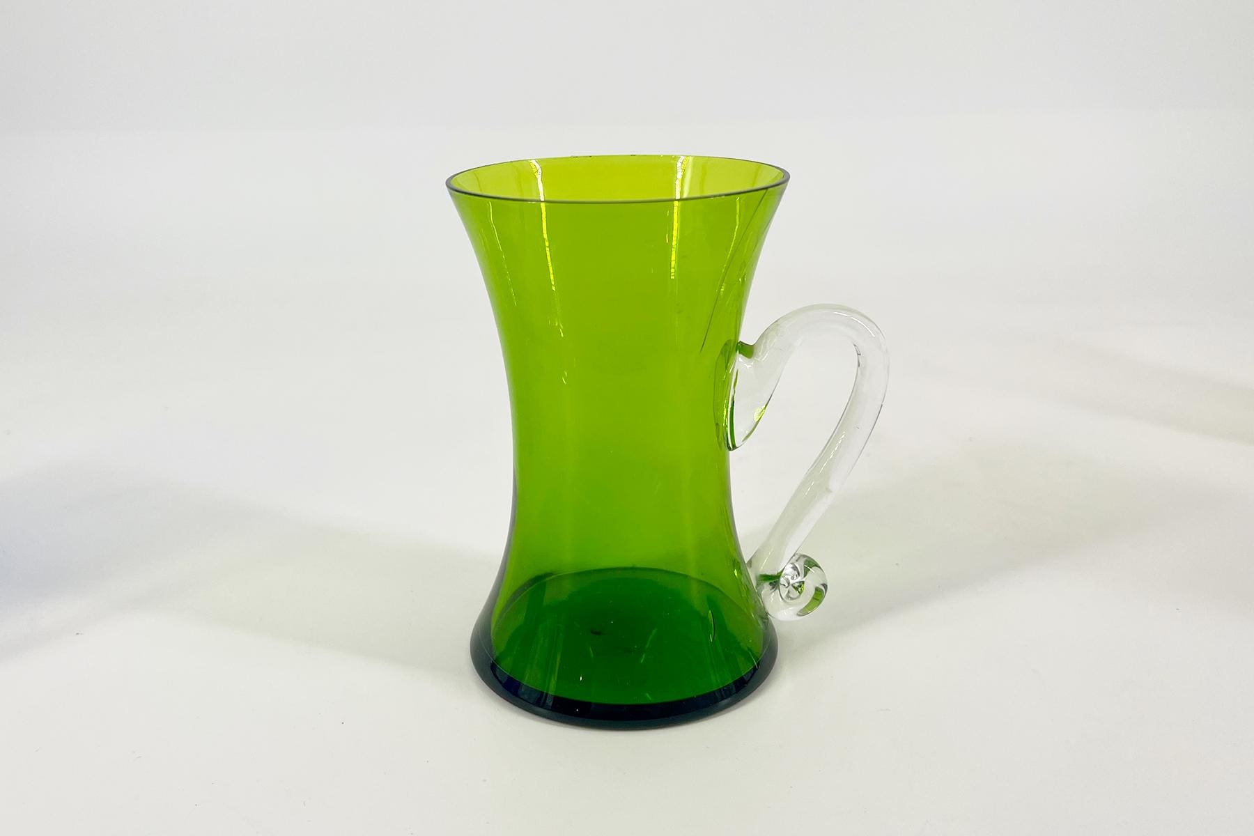 Green glass pitcher with a clear curved handle on a white background (empty).