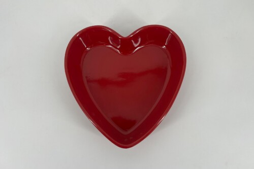 Red heart-shaped ceramic plate on a light background, viewed from above.