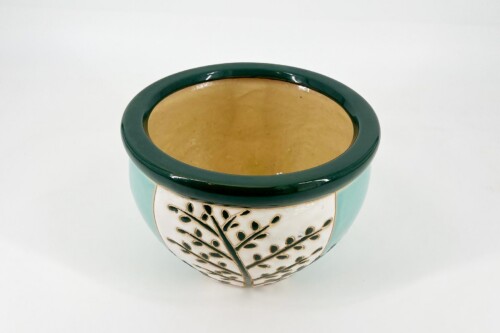 Decorative ceramic planter with teal exterior, dark green rim, and cream leaf-pattern panel on white background