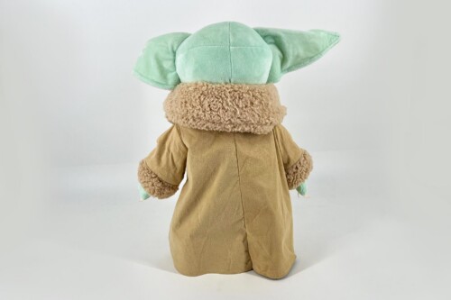 Back view of a Grogu plush toy wearing a tan robe, with green ears sticking out to the sides.