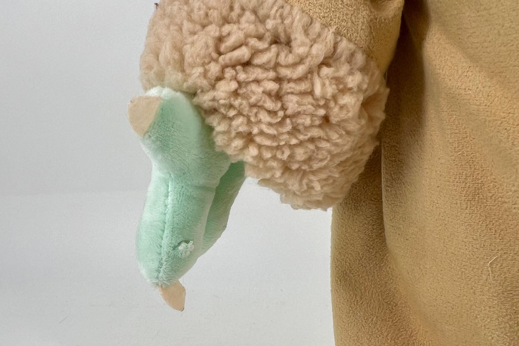Close-up of a beige plush toy showing its fluffy body and a mint-green limb hanging down.