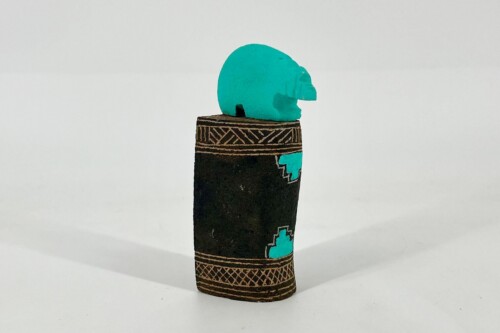Turquoise abstract sculpture perched on a carved dark wooden post with geometric patterns.