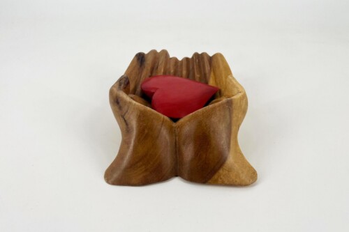 Wooden hands cupped together holding a red heart, symbolizing care and compassion.