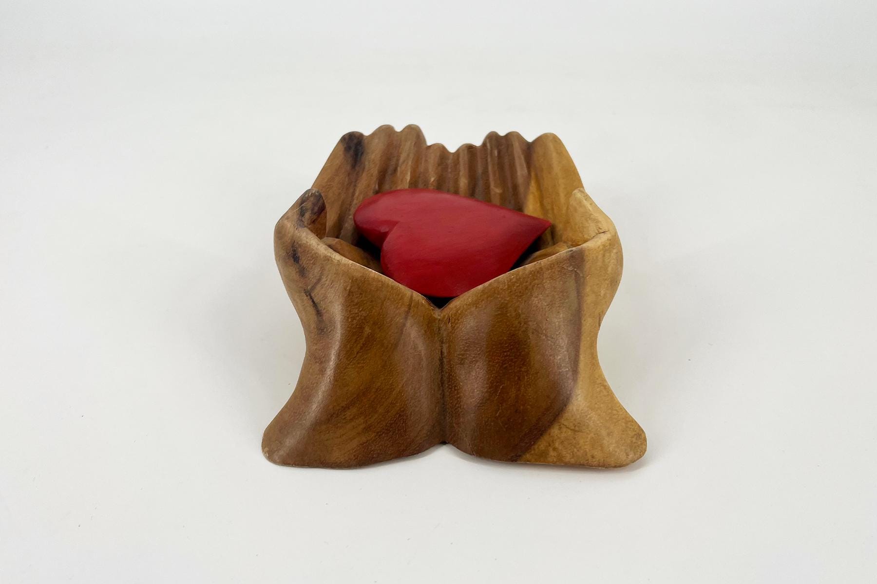 Wooden hands cupped together holding a red heart, symbolizing care and compassion.