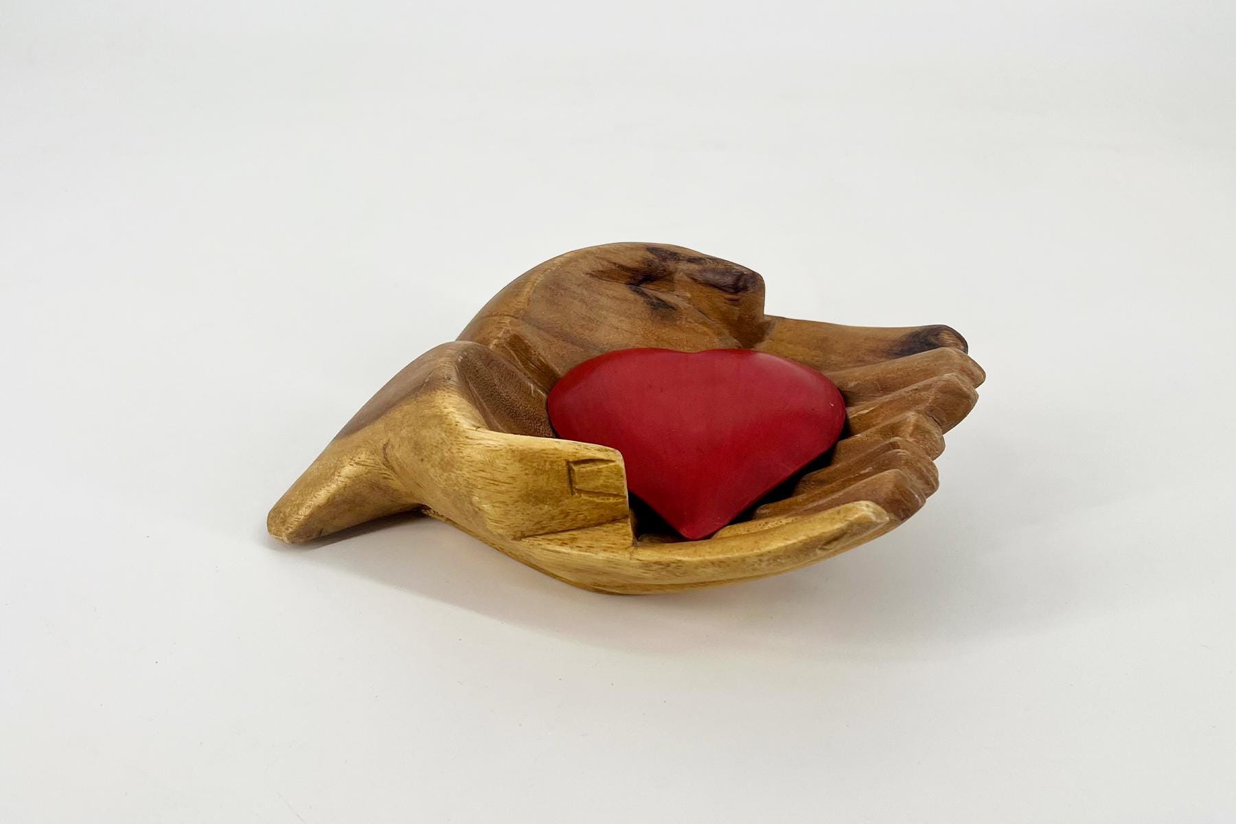 Carved wooden hands cupping a red heart in a gentle cradle sculpture.