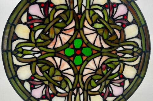 Close-up of a circular stained-glass panel with intertwining green vines, pink and cream petals, and small red accent dots.