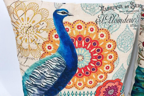 Decorative cushion featuring a blue peacock against vibrant mandala and floral patterns in warm colors.