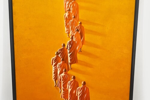 Line of Buddhist monks in orange robes walking single file along an orange path or background.