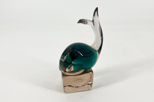 Glass sculpture of a teal bird with clear wings perched on a pinkish base.