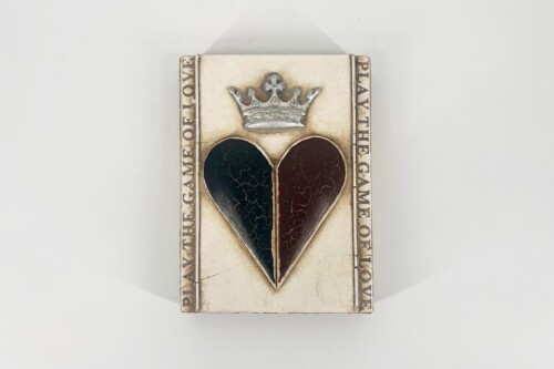 Rectangular plaque with a silver crown above a split heart (left black, right dark burgundy) on a pale background.