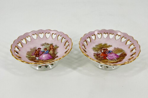Pair of pink porcelain bowls with gold scalloped rims and heart cutouts, each with a romantic painted scene.