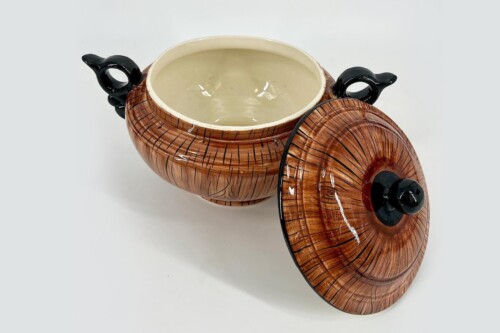 Brown ceramic lidded pot with black handles, interior glazed in light color, lid resting nearby on white surface