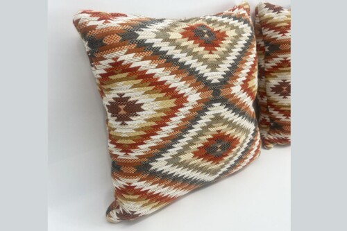 Decorative throw pillow with a geometric southwestern zigzag pattern in red, orange, cream, and gray on a light background