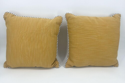 Pair of mustard-yellow throw pillows with navy-white braided piping on a white background.