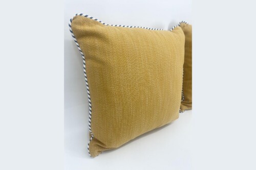Mustard yellow throw pillow with navy piping resting on a white surface.