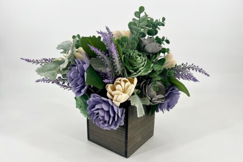 Bouquet of purple and cream flowers with green succulents in a square dark wooden vase.