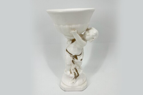 White ceramic statue of a chubby child lifting a large bowl above its head, standing on a pedestal.