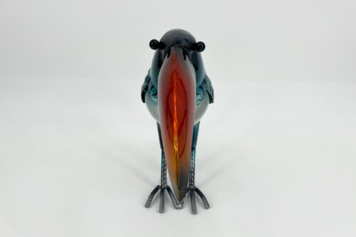 Front view of a colorful glass bird sculpture with a long bright orange beak, standing on metal legs against a white background.