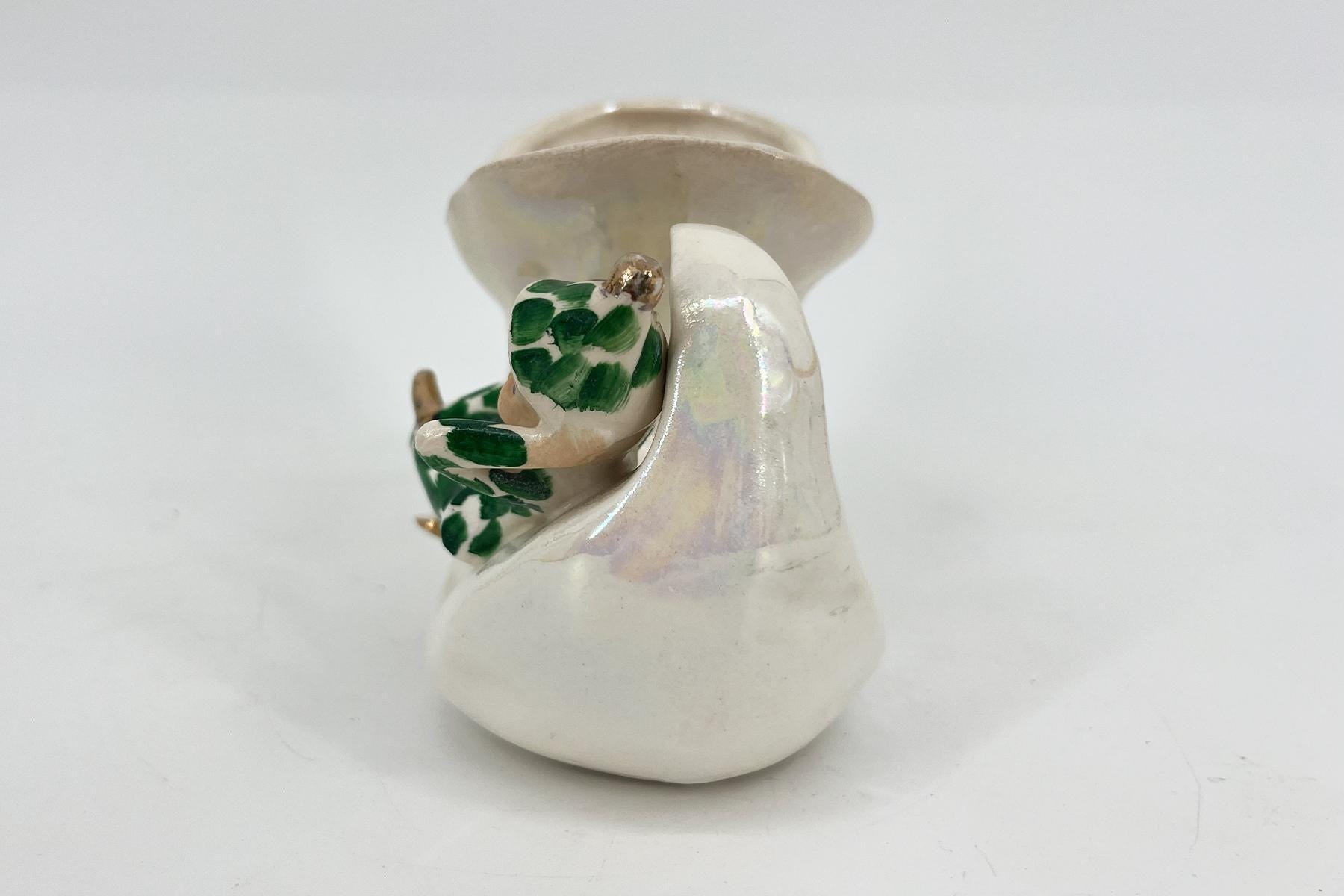 White ceramic figurine with a wide-brim hat, holding a green-leafed object close to the chest.