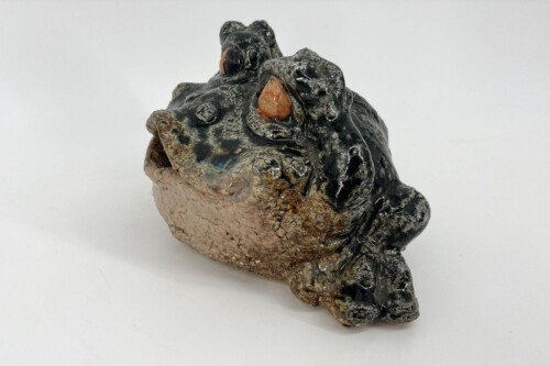 Abstract ceramic sculpture resembling a dark, glossy creature head with orange accents on a rough, earthy base.