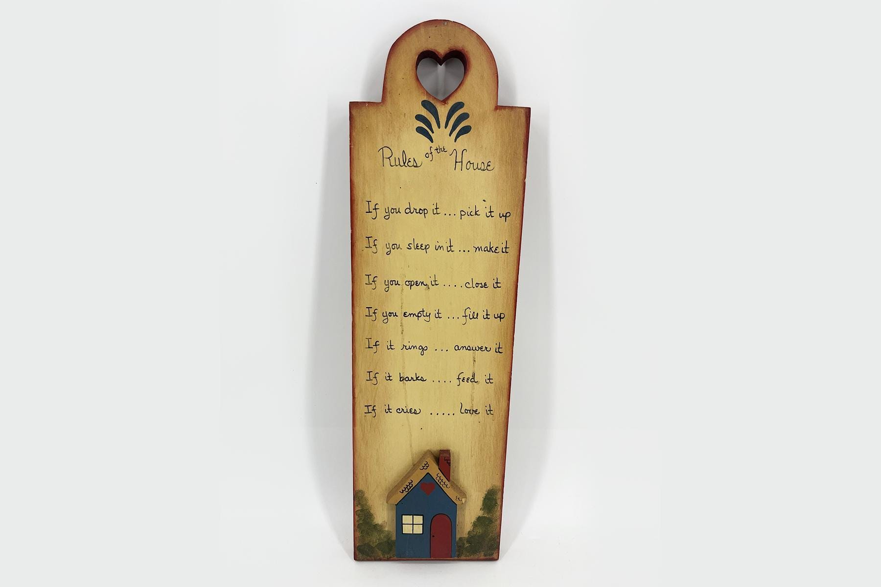 Wooden house-shaped sign titled 'Rules of the House' with a heart cutout, listing home rules in handwriting-style text on a light wood background.