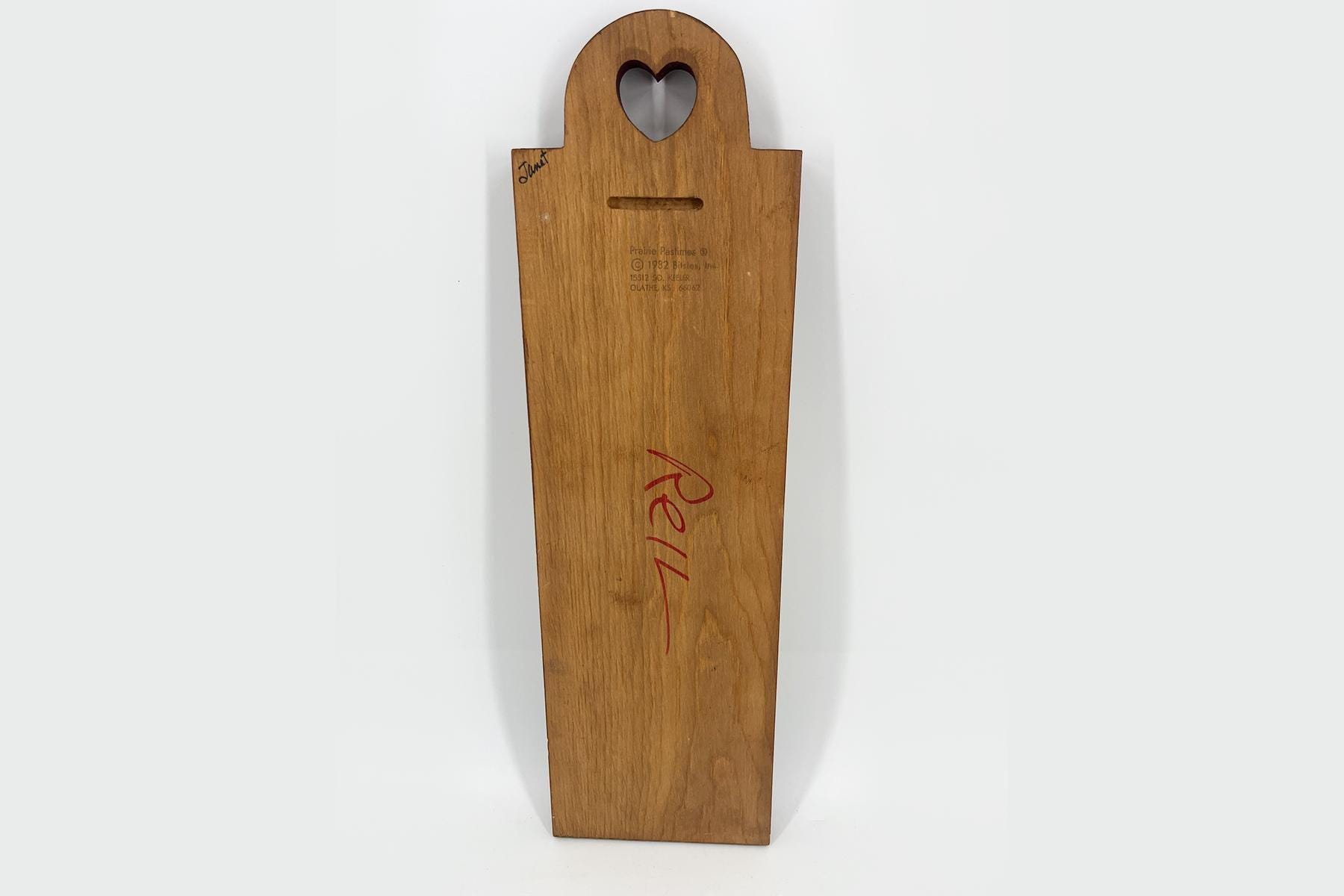 Tall wooden paddle with a heart-shaped cutout at the top and a narrow slot, featuring red handwriting along the grain.