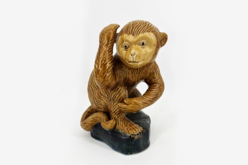 Brown monkey sculpture crouching on a dark rock pedestal, with its right hand touching its head.