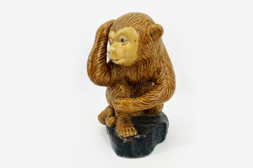 Bronze-orange orangutan statue seated on a dark rock pedestal, one hand resting on its head and the other on its knee.