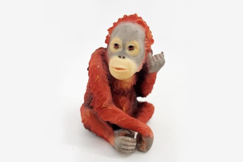 Plastic orangutan figurine with orange fur and grey face, seated with one hand raised toward the viewer